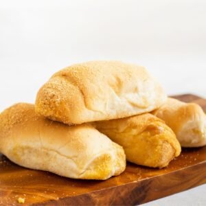 Comer pão francês engorda? A imagem mostra pães dispostos sobre uma tábua de madeira.