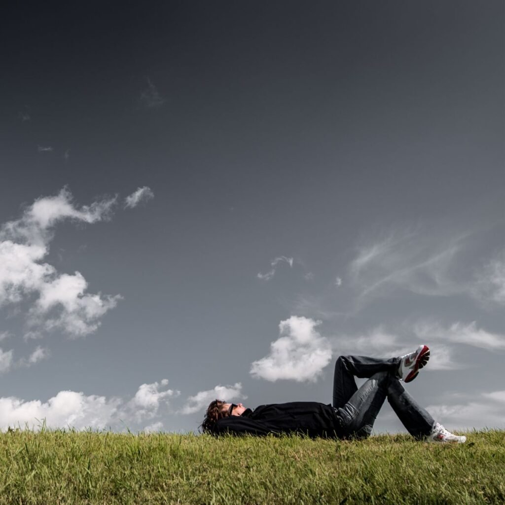 A contemplação da natureza traz paz e tranquilidade para a mente. A imagem traz um homem deitado sobre a grama, obaervando o céu.