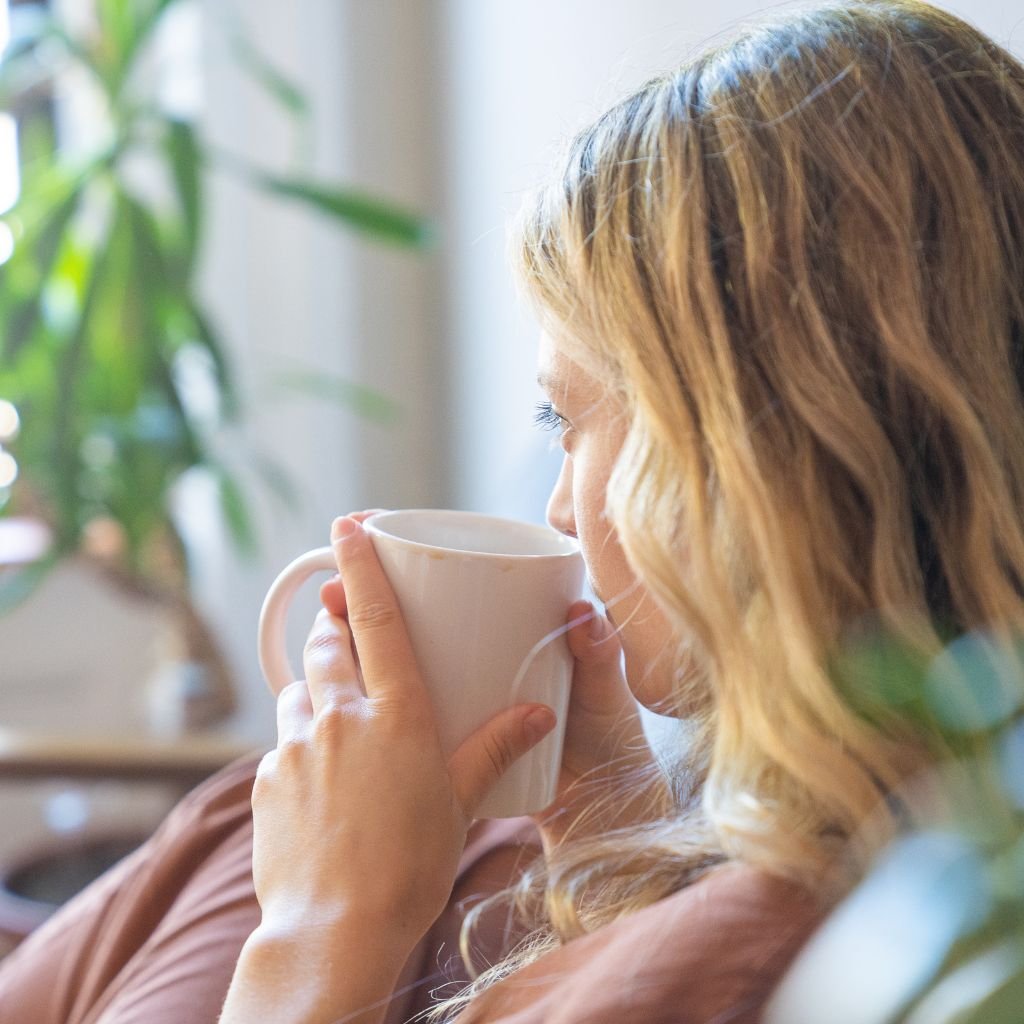 A imagem mostra uma moça saboreando uma xícara de café.